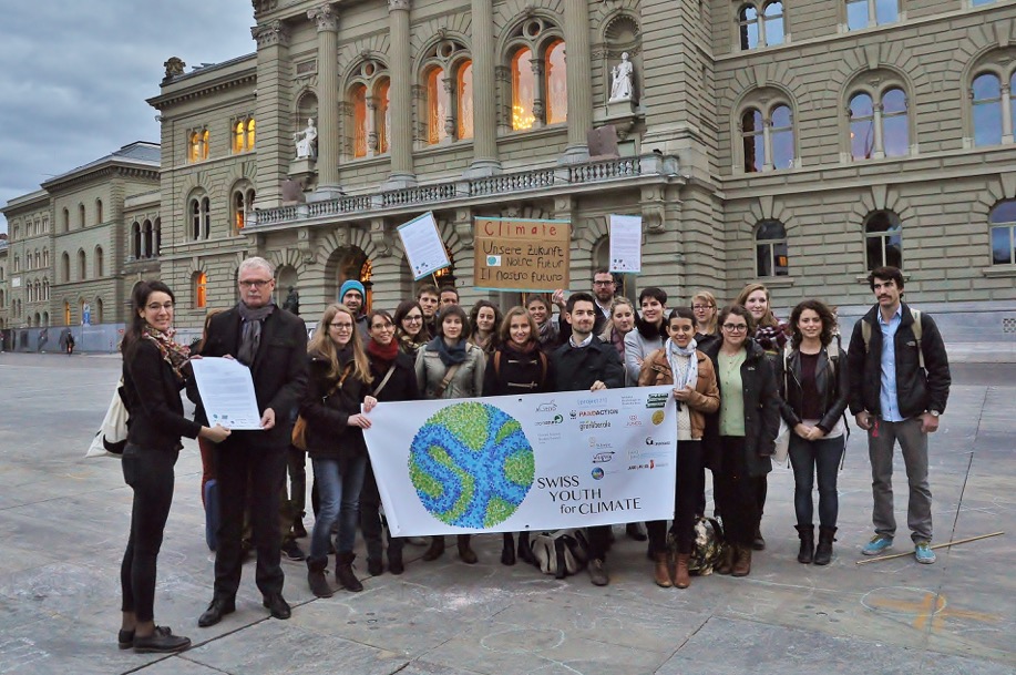 Picture of a group of students infront of the Bundeshaus holding the logo of  the "Swiss youth for climate".